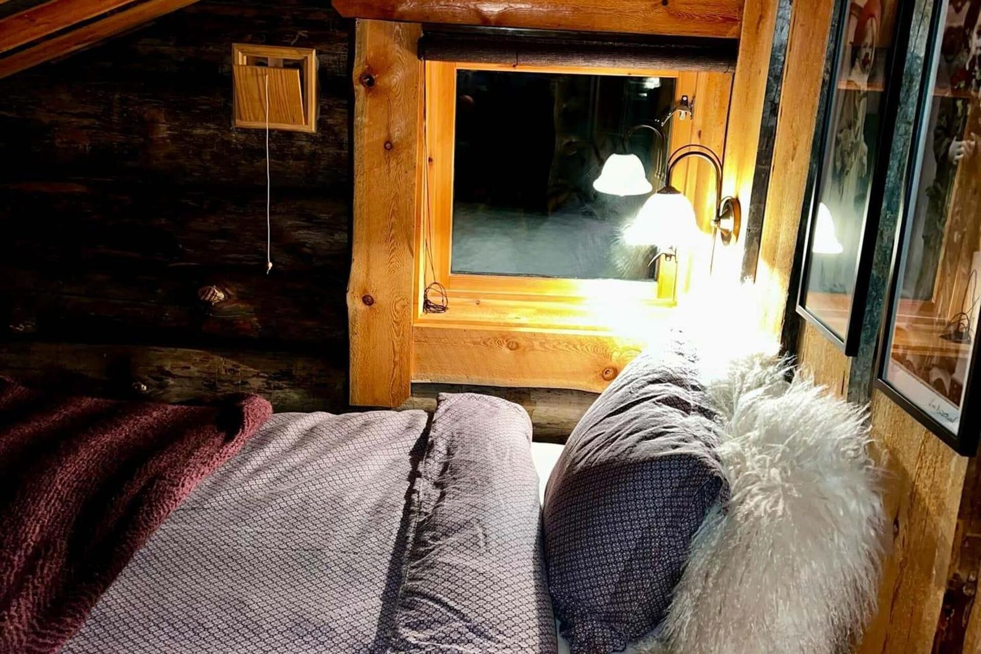 A cozy log cabin room with a bed, a window, and a lamp.