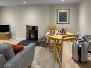 A cozy living room with a fireplace, a dining table with chairs, a sofa, a television, and a kettle.