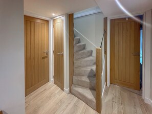 A hallway with wooden doors, a carpeted staircase, and a light-colored floor. - 2 bedroom accommodation in Aboyne (Aboyne)