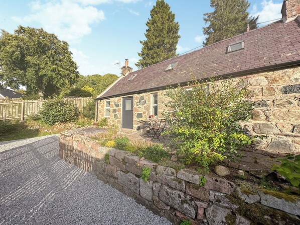 A stone cottage with a gravel driveway, a small garden, and a stone wall.