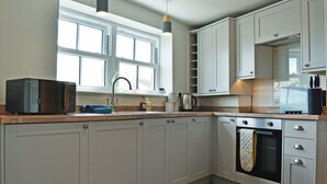 Une cuisine moderne avec des meubles gris, un four encastré et une fenêtre au-dessus de l’évier.