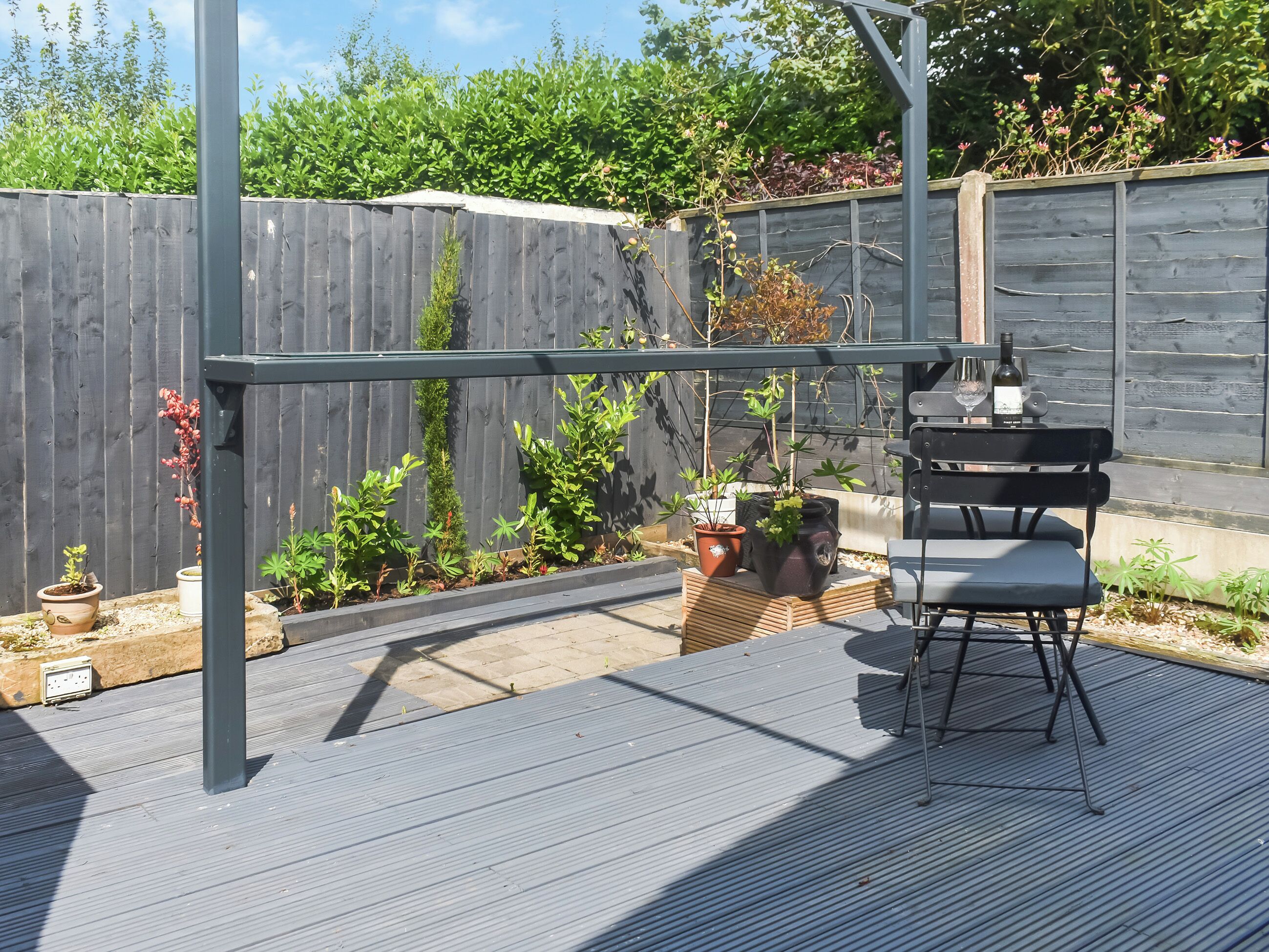 A covered outdoor patio with a metal pergola, a black metal bench, and potted plants.