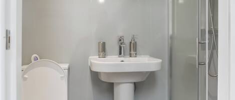 Un baño moderno con lavamanos, inodoro y ducha blancos.