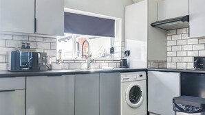 A modern kitchen with a built-in washing machine, a window with a view of a brick building, and a trash bin. - 1 bedroom accommodation in Clitheroe (Clitheroe)