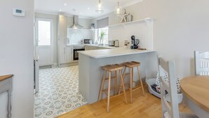 A modern kitchen with white cabinetry, a central island with stools, a microwave, and a coffee machine. - 4 bedroom accommodation in Balintore (Balintore)