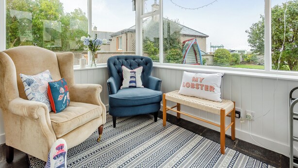 A room with a large window, a blue armchair, a beige armchair, a small bench, and a decorative pillow. - 4 bedroom accommodation in Balintore (Balintore)