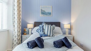 A neatly made bed with rolled towels, a headboard, and a painting of a seascape. - 4 bedroom accommodation in Balintore (Balintore)