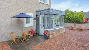 A house with a covered patio, a stone wall, and a gravel driveway. - 4 bedroom accommodation in Balintore (Balintore)