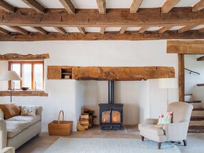 A cozy room with a wooden ceiling, a fireplace, a sofa, a chair, and a window.