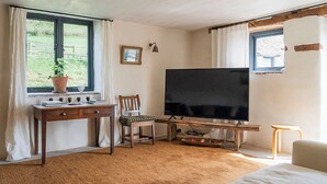 Una stanza con una grande TV a schermo piatto, una scrivania in legno, una sedia, un letto e una finestra con tende.
