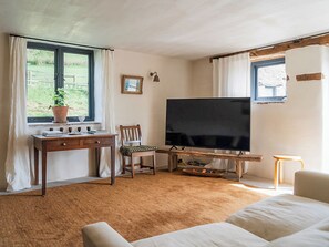 A room with a large flat-screen TV, a wooden desk, a chair, a bed, and a window with curtains.