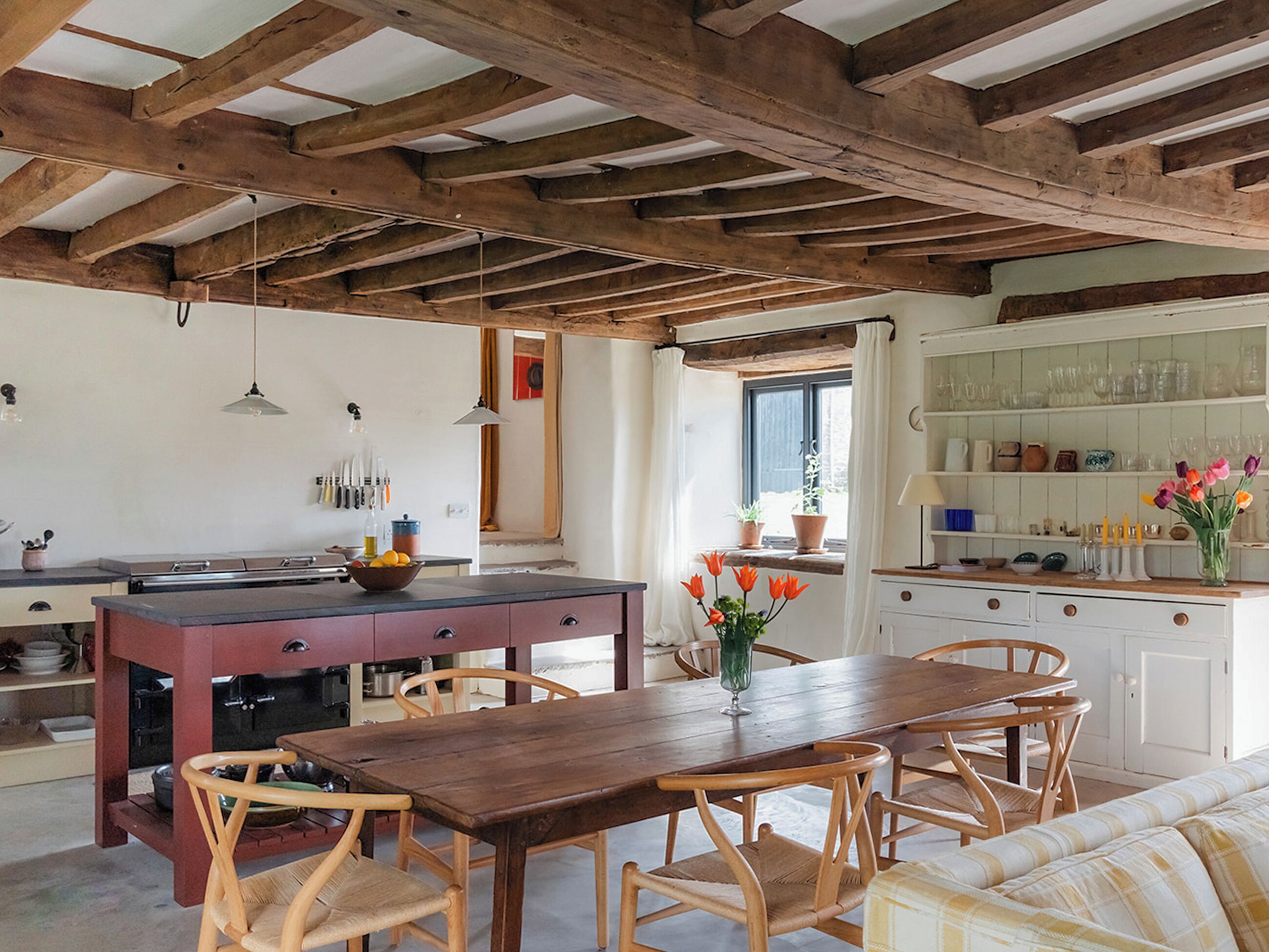 Una cocina rústica con vigas de madera, una mesa de comedor, sillas y vistas al exterior.