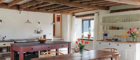 Una cocina rústica con vigas de madera, una mesa de comedor, sillas y vistas al exterior.