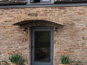 A stone building with a dark door, two potted orange flowers, and a small awning above the door.