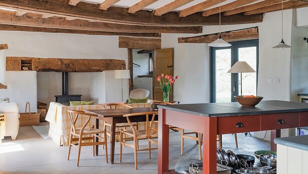 Una cucina rustica con travi in legno, un'area pranzo con sedie di legno, un tavolo e un fornello.
