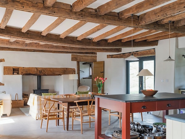 A rustic kitchen with wooden beams, a dining area with wooden chairs, a table, and a stove.