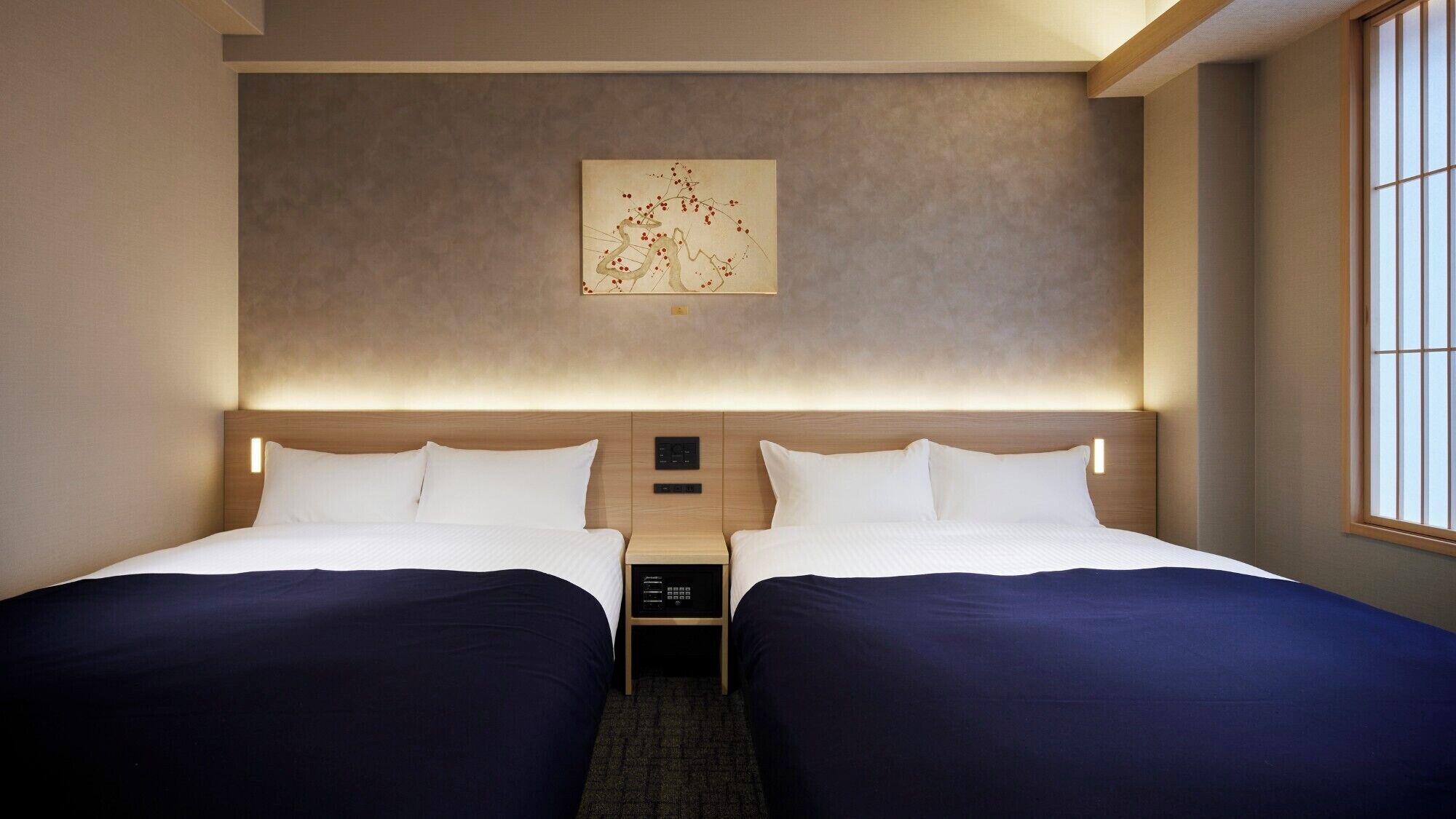 Une chambre d’hôtel avec deux lits, une table de chevet, une œuvre d’art accrochée au mur et une fenêtre avec des stores.