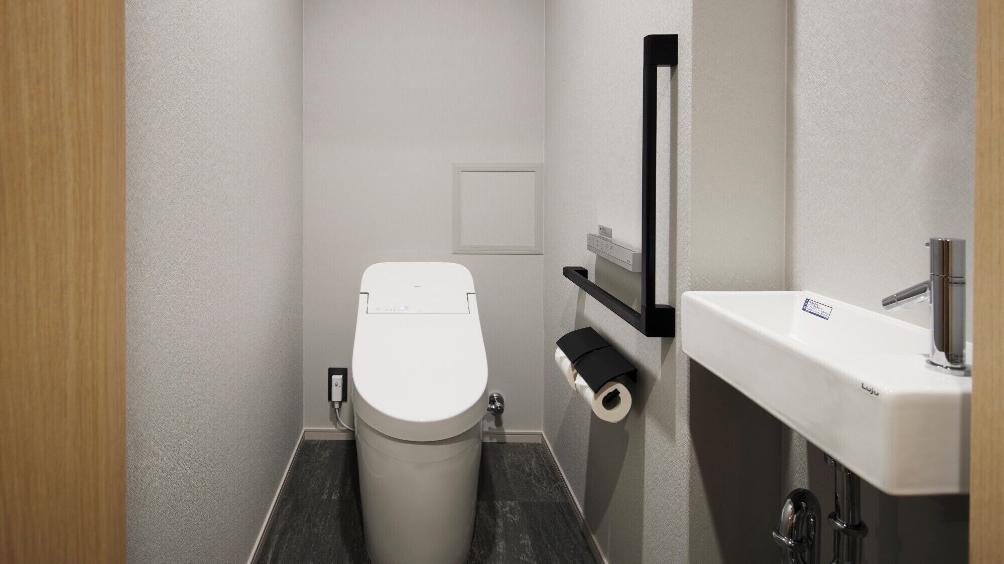 A compact bathroom with a white toilet, a black toilet paper holder, and a white sink with a chrome faucet.