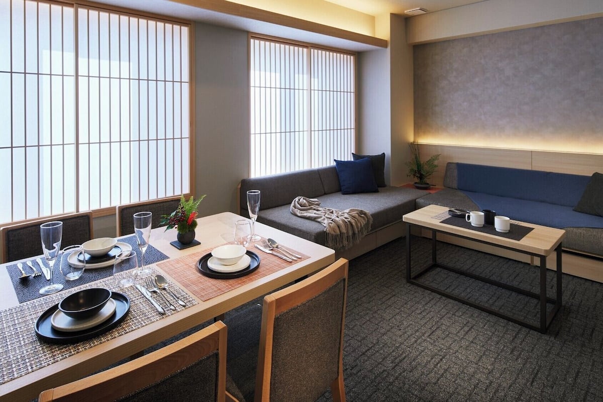 A modern, well-lit room with a dining table set for two, a sofa, and a small coffee table.