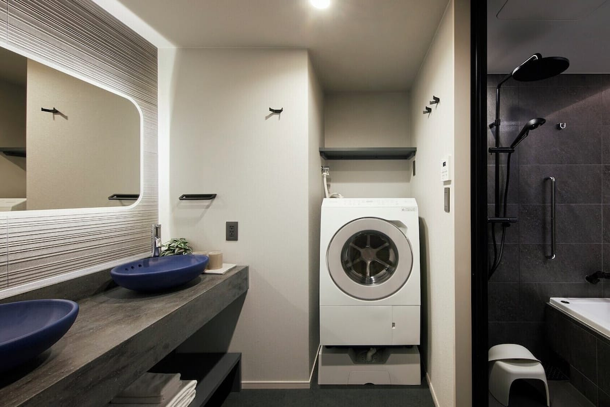 A modern bathroom with a large mirror, a washing machine, a bathtub, and a shower area.