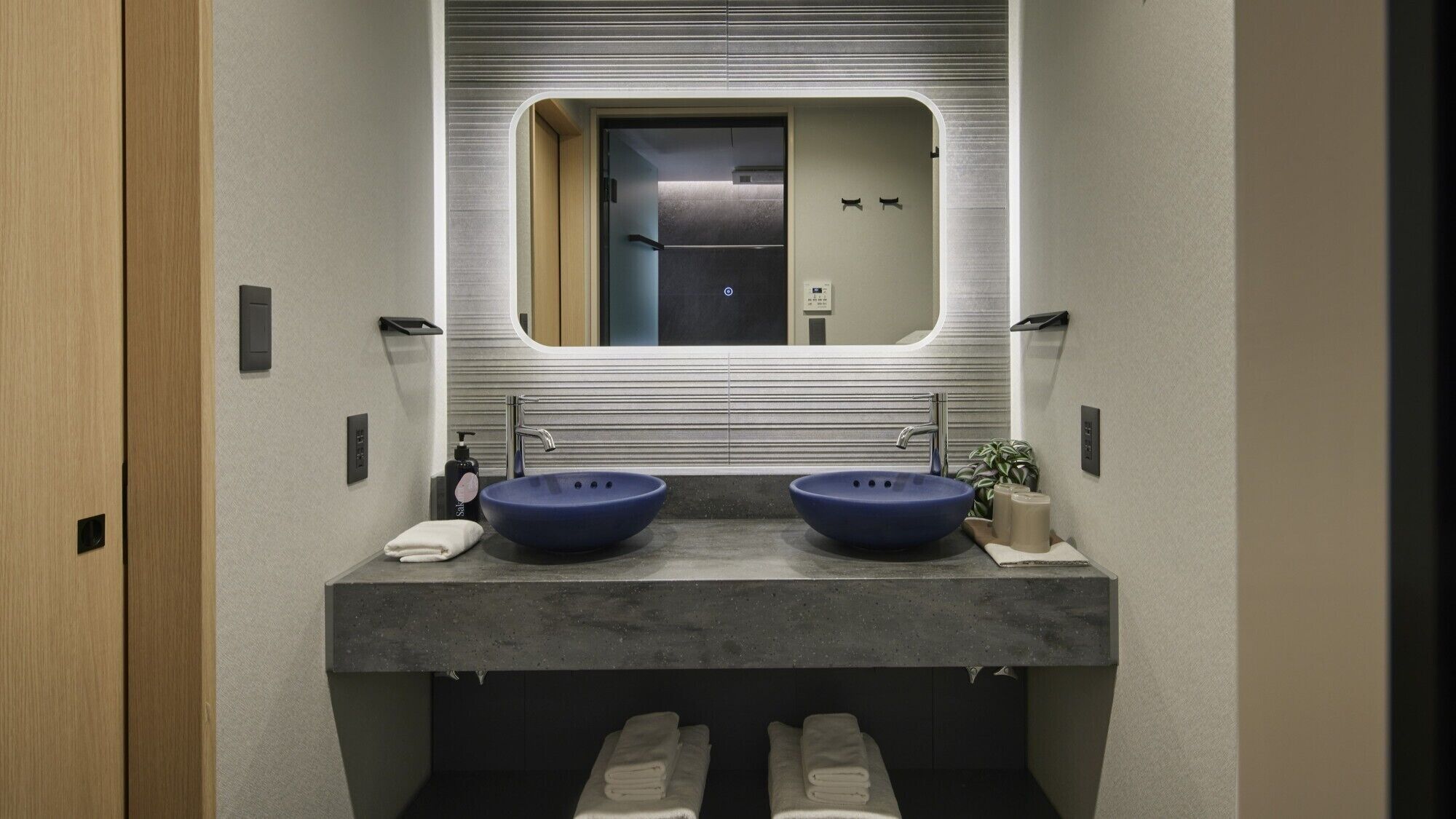 A modern bathroom with two sinks, a large mirror, and a towel rack.