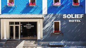 A hotel with a blue facade, a welcome sign, and flower boxes on the windows. - Solief Hotel (Tashkent)
