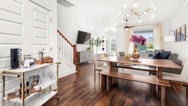 A modern kitchen with a wooden dining table, a bar cart, and a TV mounted above the counter.