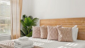 A neatly made bed with a wooden headboard, a potted plant, and a window with blinds.