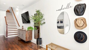 A modern living room with a staircase, a large mirror, and a collection of hats on the wall.