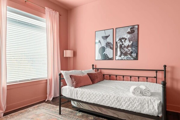 A bedroom with a bed, pink walls, and two framed pictures on the wall.