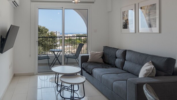 A modern living room with a grey sofa, two white round tables, and a balcony with a view of the sea. - Phaedrus Living: Golden Seaview Residence (Paphos)