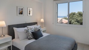A bedroom with a bed, two bedside tables, a window with a view, and two framed pictures on the wall. - Phaedrus Living: Golden Seaview Residence (Paphos)