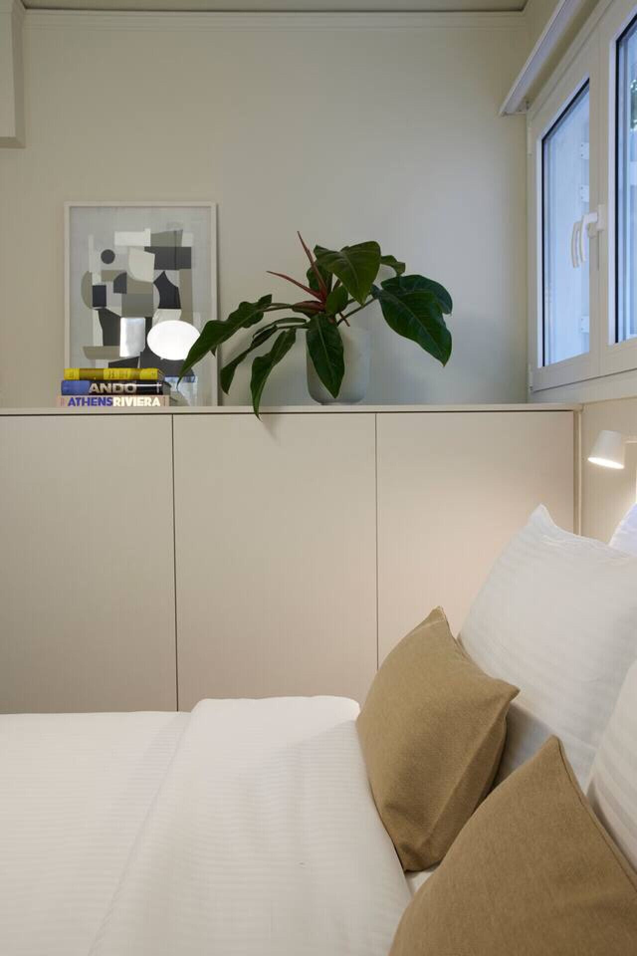 A neatly arranged hotel room with a bed, pillows, a potted plant, and a framed artwork on the wall.
