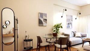 Ein modernes Wohnzimmer mit einem Glastisch, zwei Stühlen, einem Sofa und einem Couchtisch. Auf dem Tisch steht ein Blumentopf und ein Beistelltisch mit einer Lampe.
