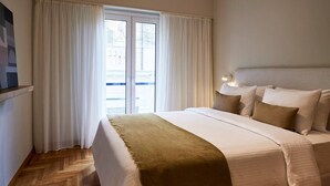 Una habitación de hotel con cama, cortinas, una ventana y una lámpara fijada a la pared.