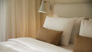 Una cama bien hecha con almohadas blancas y marrones, un cabecero blanco y una lámpara de noche.