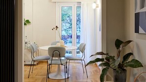 Una sala de estar moderna con comedor, piso de madera, un ventanal con cortinas y una planta en maceta.