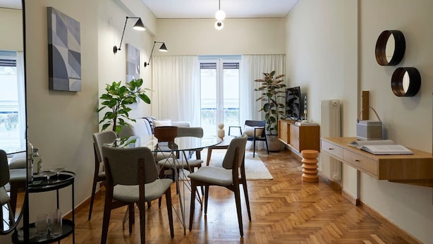 Una sala de estar moderna con una mesa de comedor de vidrio, asientos cómodos, una planta grande y un mueble de madera con un radio.