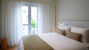 Habitación de hotel con una cama grande, cortinas blancas, una planta en maceta y vistas al exterior.