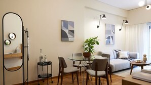Una sala de estar moderna con una mesa de comedor de vidrio, un sofá y una mesa de centro. Hay dos sillones, una planta en maceta y obras de arte en las paredes.