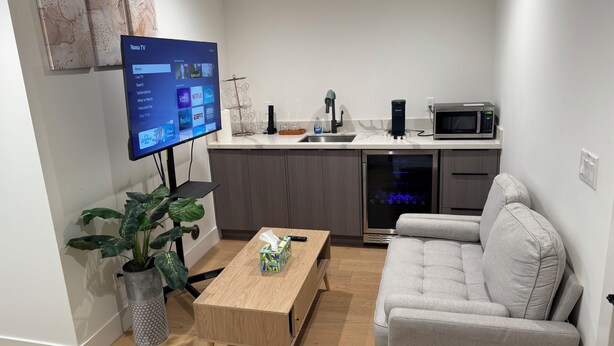 Een moderne woonkamer met een flatscreen televisie, een grijze bank, een houten salontafel en een potplant.