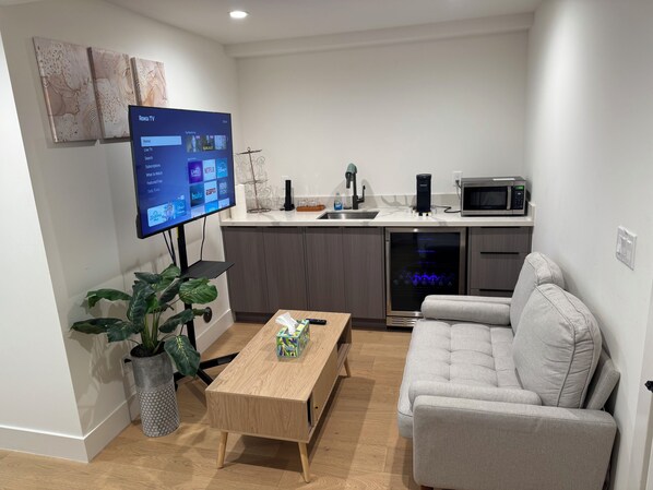 A modern living room with a flat-screen TV, a grey sofa, a wooden coffee table, and a potted plant.