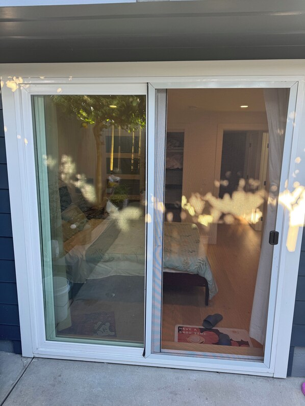 A sliding glass door leading to a room with a bed, a small table, and a chair.