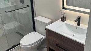 Een moderne badkamer met een glazen douchecabine, toilet, wastafel met spiegel en houten kastjes.