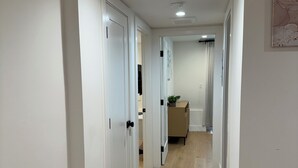 Een gang met witte muren en houten vloeren, die leidt naar een kamer met een bed en een raam.