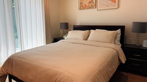 Een net opgemaakt bed met een hoofdbord, twee nachtkastjes met lampen en twee ingelijste kunstwerken aan de muur.