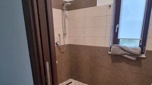 Une salle de bain avec une douche, une fenêtre et des toilettes.