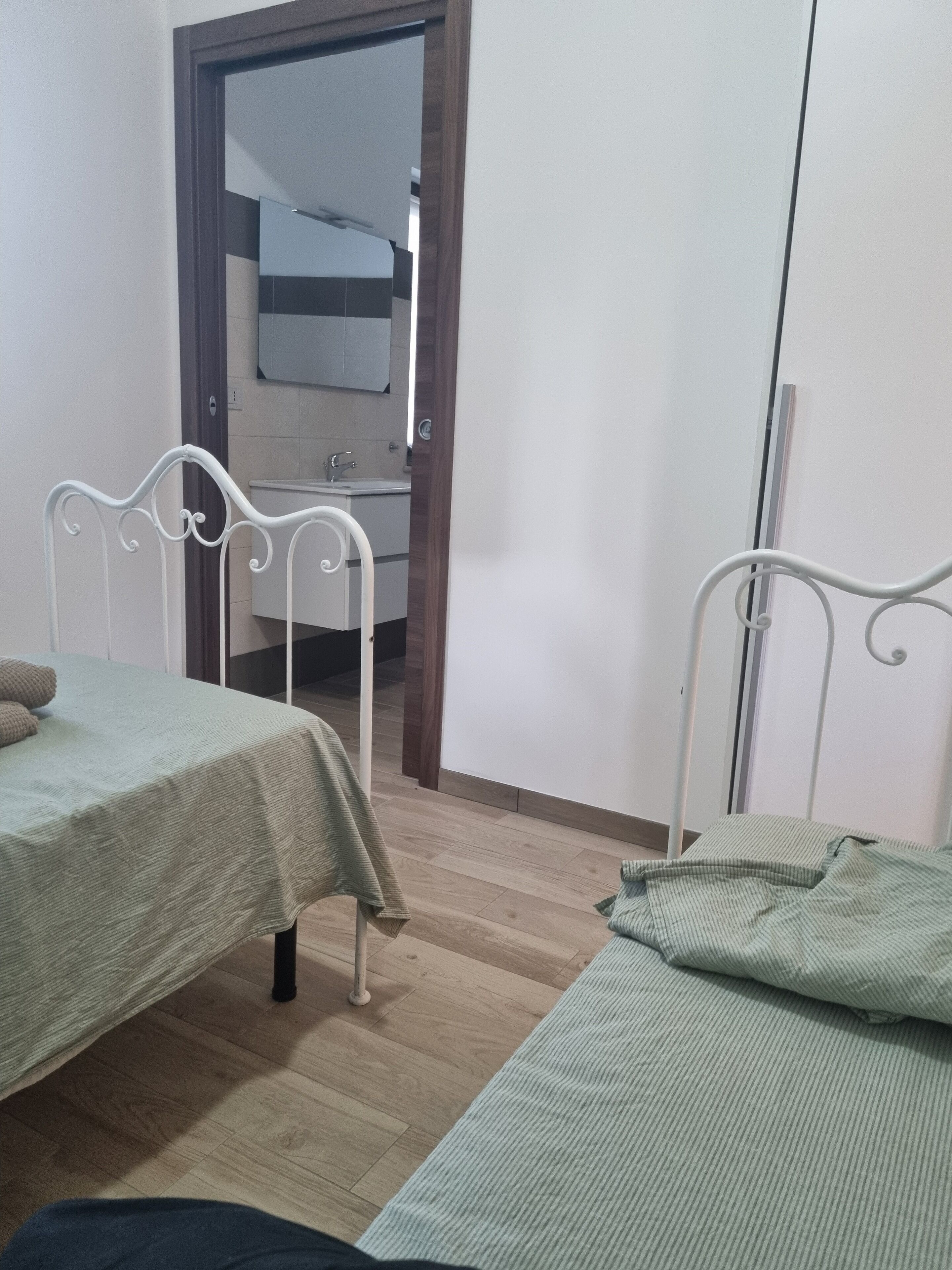 Una habitación con dos camas, suelo de madera y una puerta que da a un baño.