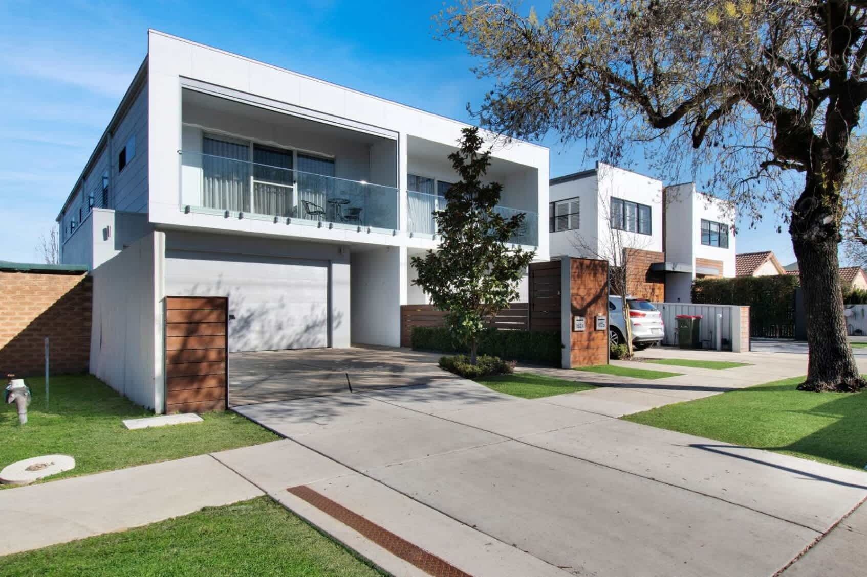 A modern two-story residential building with a garage, a covered patio, and a well-maintained lawn.