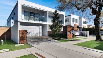 A modern two-story residential building with a garage, a covered patio, and a well-maintained lawn.